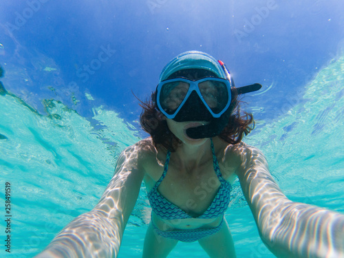 woman taking an underwater selfie while snorkeling in crystal clear tropical water