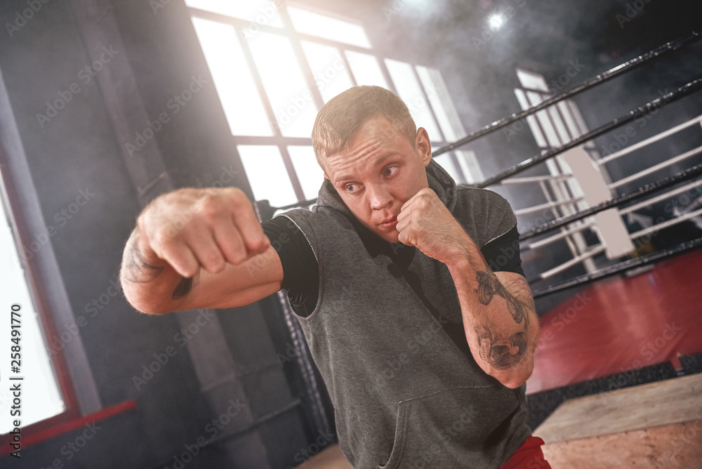 Power hook to the head. Close-up of confident handsome athlete in sports  clothing throwing hook punch opposite boxing ring Stock Photo