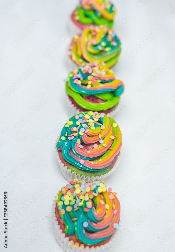 beautiful, bright, very colorful muffins decorated with rainbow cream and candy confetti, on a bright background
