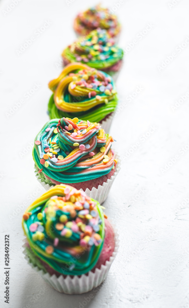 beautiful, bright, very colorful muffins decorated with rainbow cream and candy confetti, on a white background