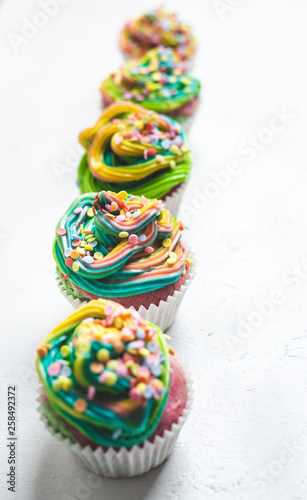 beautiful, bright, very colorful muffins decorated with rainbow cream and candy confetti, on a white background © Auslander
