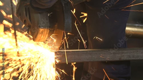 Man with a disc grinder cutting a rectangular metallic tube with yellow sparkles