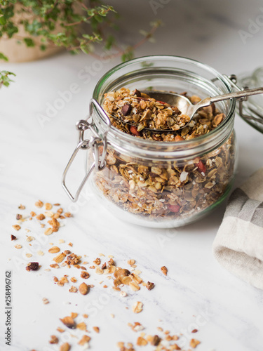 Nuts, seeds, goji berries granola in open glass jar. Healthy breakfast - homemade granola in a jar on a marble white background