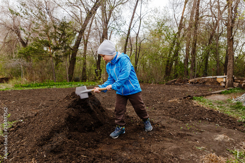 seven-year-old boy in a blue windbreaker and hat digging humus sapper shovel in the garden