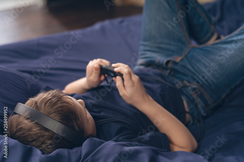 boy listening to music in headphones while lying in bed selective focus on head