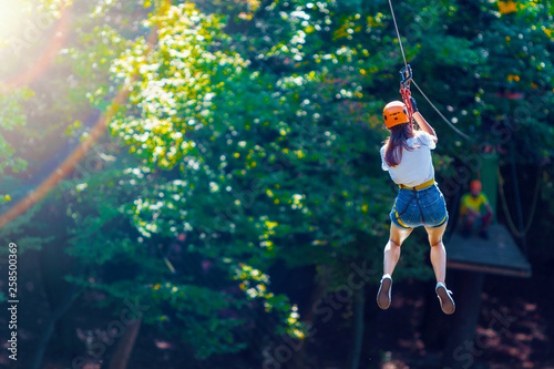 Happy women girl female gliding climbing in extreme road trolley zipline in forest on carabiner safety link on tree to tree top rope adventure park. Family weekend children kids activities concept photo