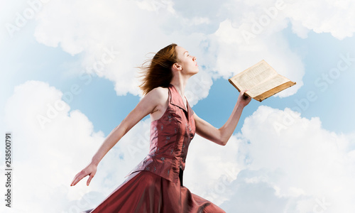 Girl against cloudy sky with opened book in palm as idea for knowledge