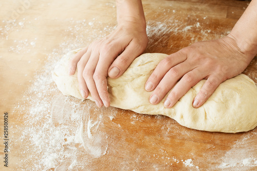 woman's hands and dough yeast lying on a wooden cutting board sprinkled with flour
