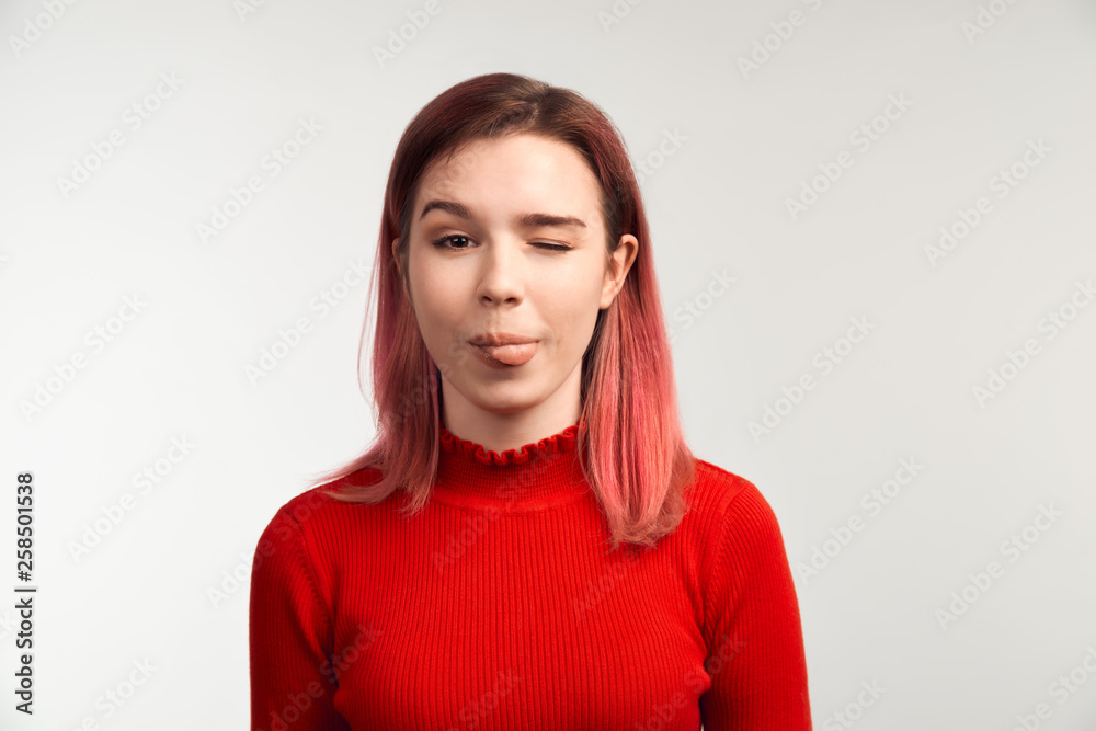 A funny girl in glasses makes faces, sticking her tongue out and winks. The concept of frivolous fun and teasing. Isolated on white background in studio A funny girl in glasses makes faces, sticking her tongue out and winks. The concept of frivolous fun and teasing. Isolated on white background in studio
