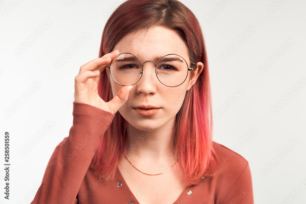 Low-spirited young student frowns after receiving a bad grade for the exam. Beautiful young woman holding glasses and squinting trying to read the inscription. Isolated on white background in Studio