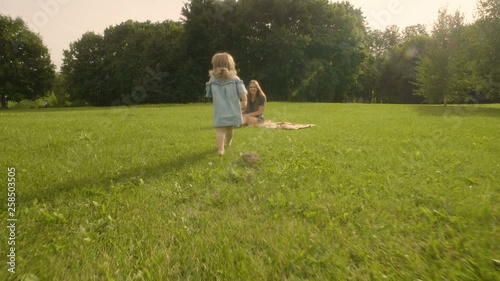 Baby girl running through the grass and rushes into mother hands in garden in sunset sunlight. Slow motion. Happy smiling baby girl.