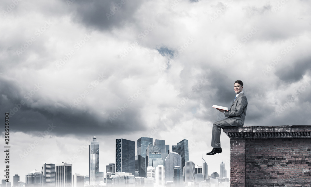 Man on roof edge reading book and cityscape at background Man on roof edge reading book and cityscape at background