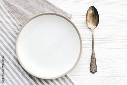 Diet concept. Stylish empty plate with vintage spoon on napkin on white table, flat lay. Modern set, serving for reception and party celebration. Copy space