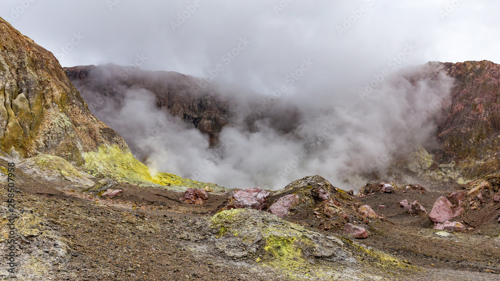 Tourists are dwarfed by the sulphurous clouds and steam that rises from the boiling lake in the vent of the crater of the active volcano - White Island, New Zealand.