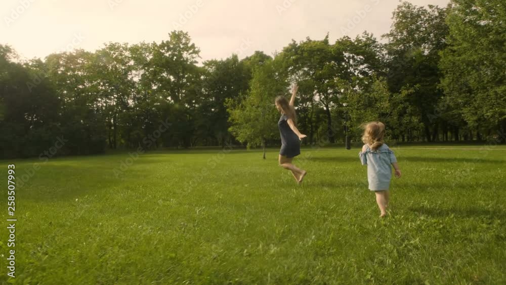 Baby girl with mother running through the grass in the summer sunlight in park. Baby have fun. Slow motion. Happy family concept. Baby girl with mother running through the grass in the summer sunlight in park. Baby have fun. Slow motion. Happy family concept.