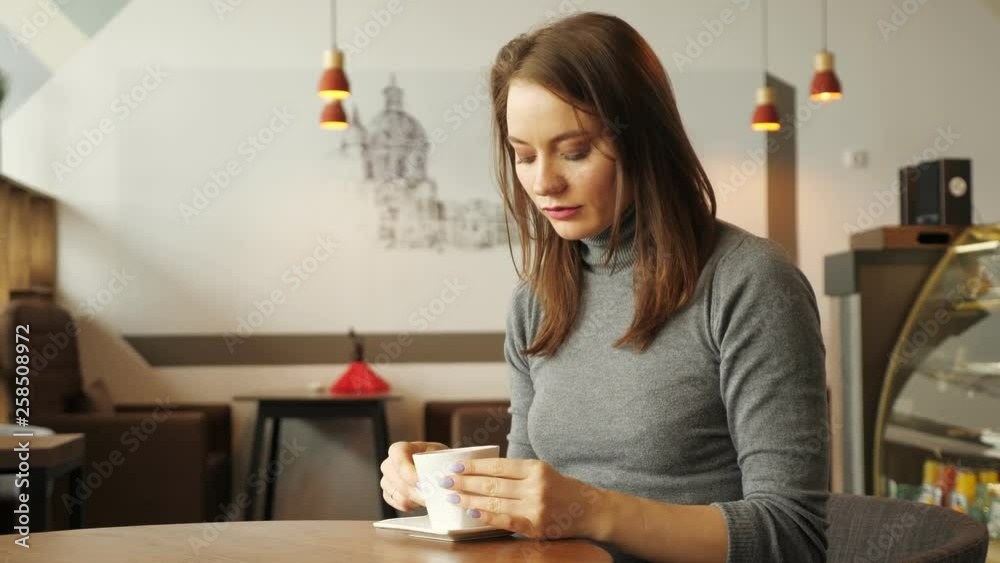 Young women is drinking a cup of coffee sitting in cafe in the city. Side view. Young women is drinking a cup of coffee sitting in cafe in the city. Side view.