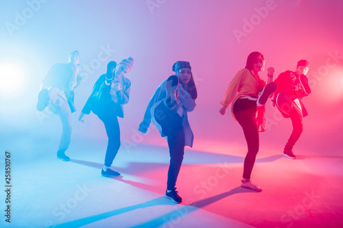 Group of male and female dancers in colorful neon light having fun dancing. Party guests enjoy atmosphere and effects in the night club. Creative fashionable neon color.