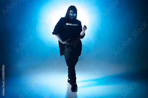 Trendy young woman dancing single in club, neon light, lots of smoke. Fashion street wear. Silhouette