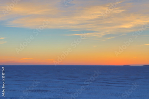 The sunset or sunrise. The cloudy sky cloured in red, orange, crimson, purple, violet and blue bright and vivid coloures with setting or rising sun over the sea, lake or bay covered with ice and snow © Майджи Владимир