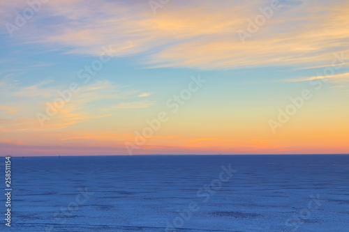 The sunset or sunrise. The cloudy sky cloured in red, orange, crimson, purple, violet and blue bright and vivid coloures with setting or rising sun over the sea, lake or bay covered with ice and snow © Майджи Владимир