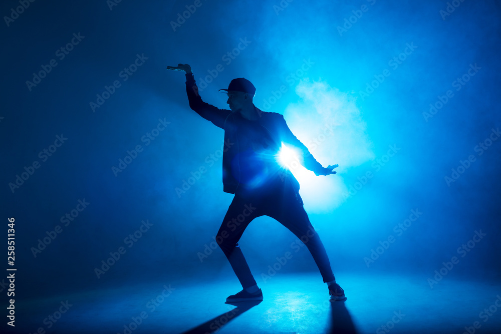 silhouette of single male break dancer isolated on blue neon background with light flare in middle