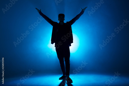 Full-size of silhouette of male break dancer performing on blue neon stage his expressive dance, Dark blue background with light flare on background