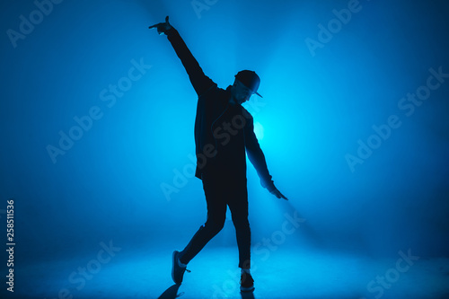 Full-size of silhouette of male break dancer performing on blue neon stage his expressive dance, Dark blue background with light flare on background © alfa27
