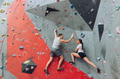 Pretty girl and handsome man giving high-five to each other at the upper level of the climbing wall. Tired girl managed to climb the wall.
