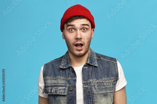 Omg. Are you kidding me? Funny cute hipster guy in stylish clothes keeping mouth wide opened expressing shock, surprise and full disbelief, amazed with astonishing news, can’t hide his true reaction photo