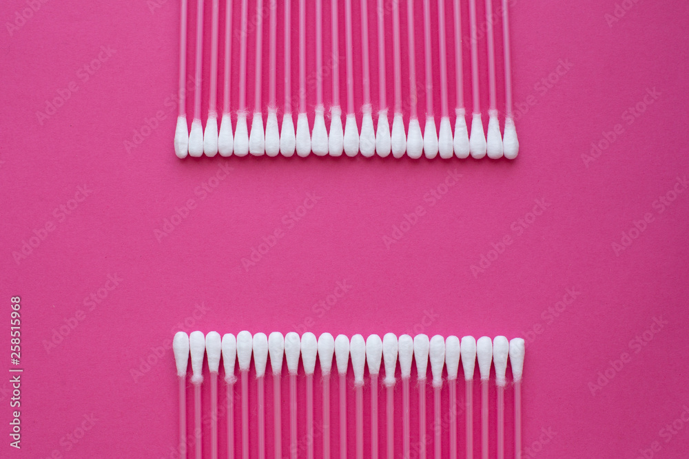 Closeup top view on cotton buds laid in a two horizontal line on pink background Closeup top view on cotton buds laid in a two horizontal line on pink background