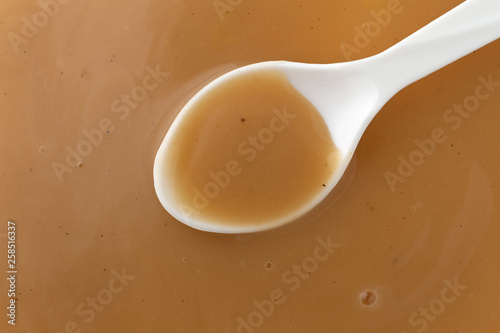 Top view of creamy brown turkey gravy with a white spoon in the food.