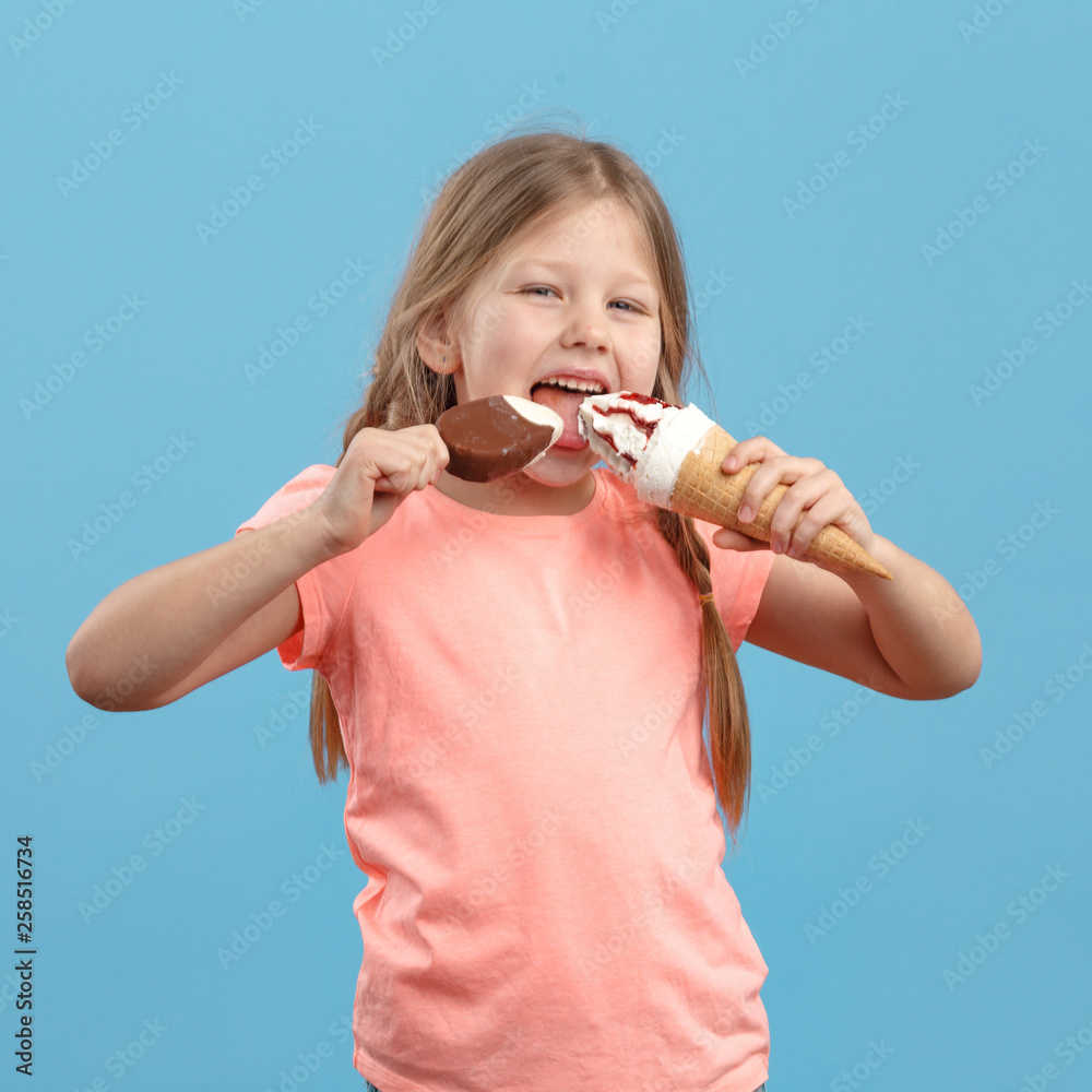 Cute little girl eats ice cream and laughs in studio over blue background Cute little girl eats ice cream and laughs in studio over blue background