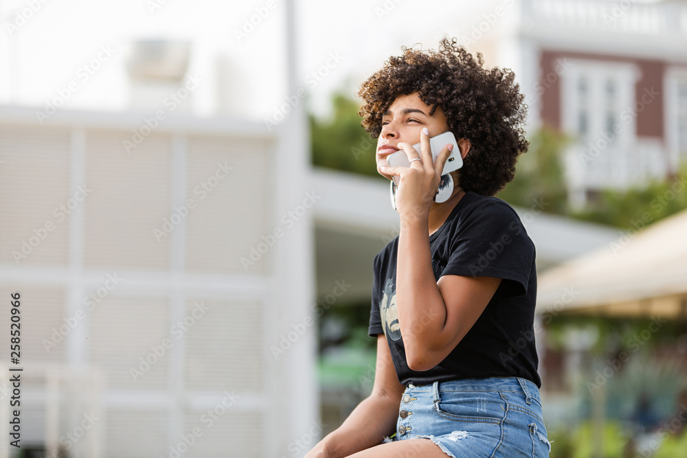Fototapeta premium Outdoor portrait of a Young black African American young woman speaking on mobile phone