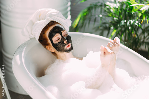 Leinwand Poster Skin care - Young lady with facial black clay mask applyed on her face relaxing