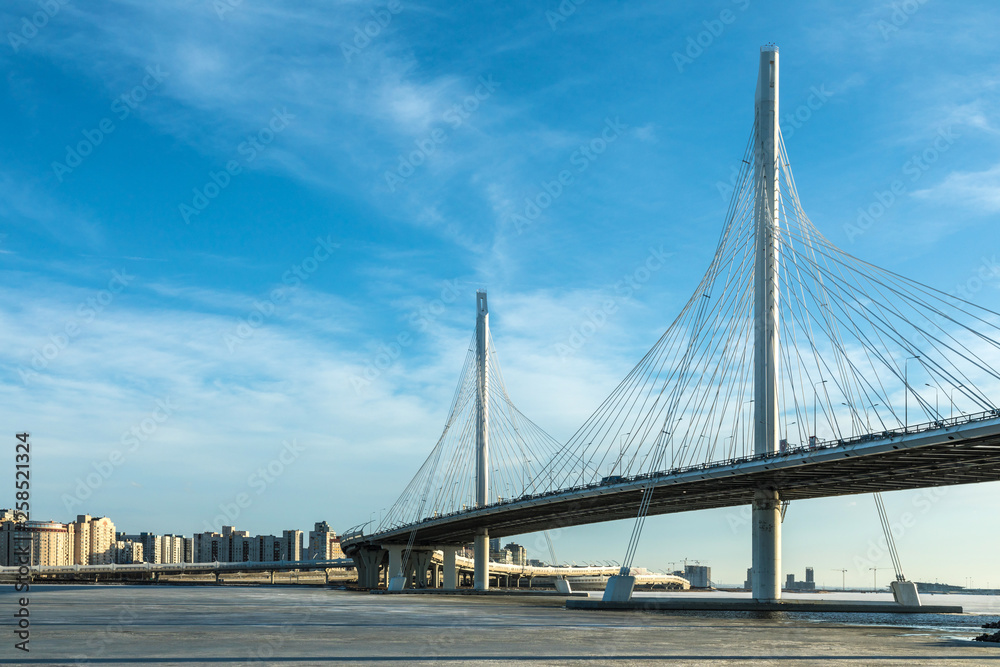 Naklejka premium The bridge of circle highway road over Neva river near the mouth of it in the clear day. The winter landscape of the river covered with ice and snow and with the sky with clouds