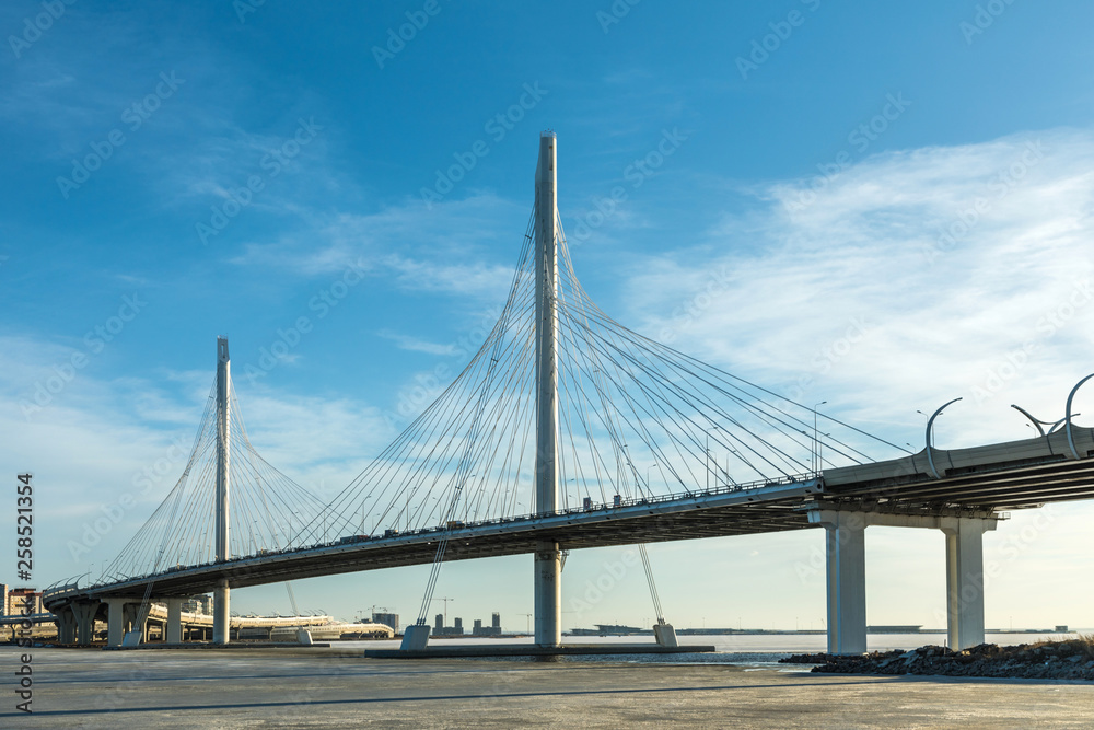 The bridge of circle highway road over Neva river near the mouth of it in the clear day. The winter landscape of the river covered with ice and snow and with the sky with clouds