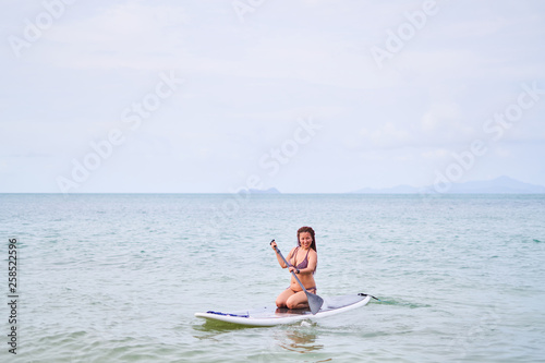 Asian girl in a bathing suit floating on the sup board and smiling