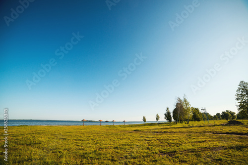 Blue sky and green trees over lake. Beautiful summer morning near lake. Water landscape. Summer vacation concept. Travel, lifestyle and nature concept.