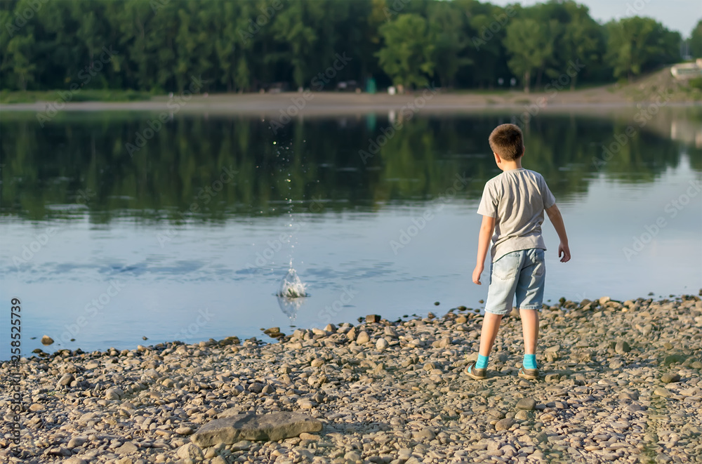 Fototapeta premium a child, a teenager, on a stony shore throws stones into the river, lake