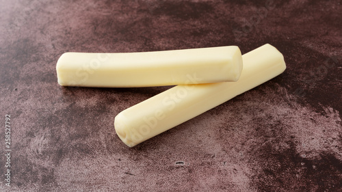 Two strands of mozzarella string cheese on a red background side view