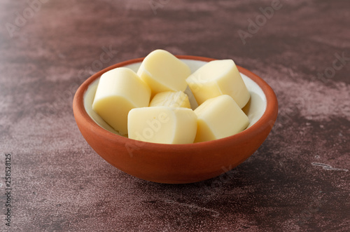 Small bowl of mozzarella string cheese pieces on a red background side view