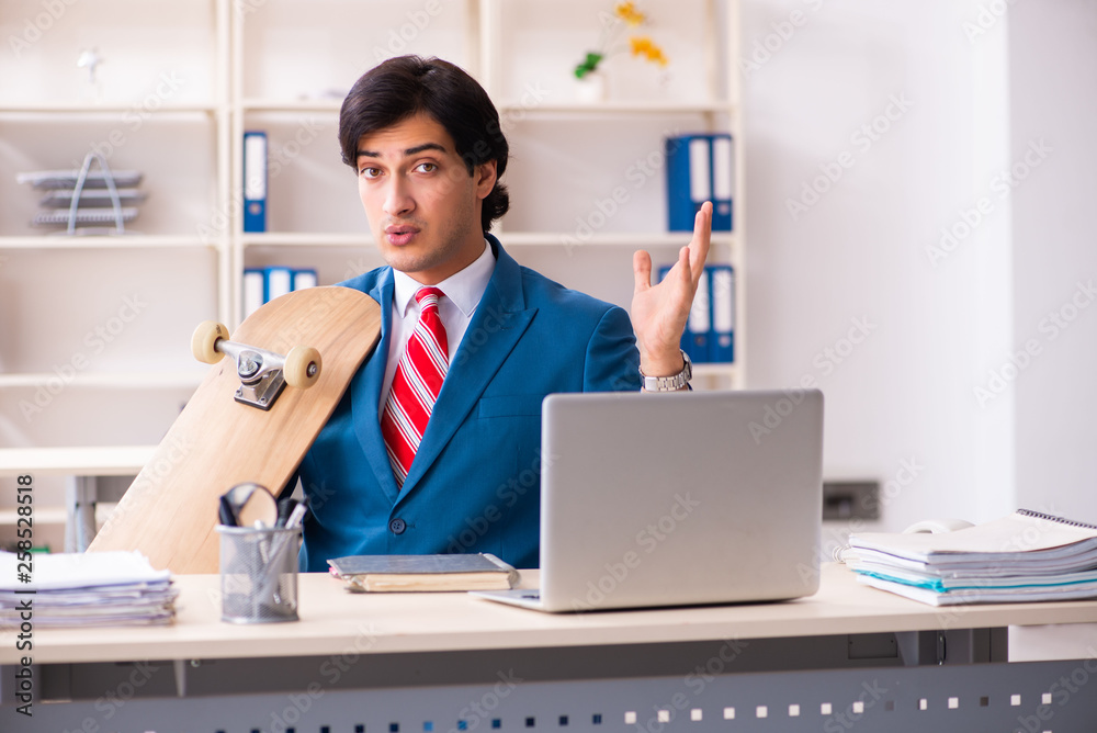 Young handsome businessman with longboard in the office 