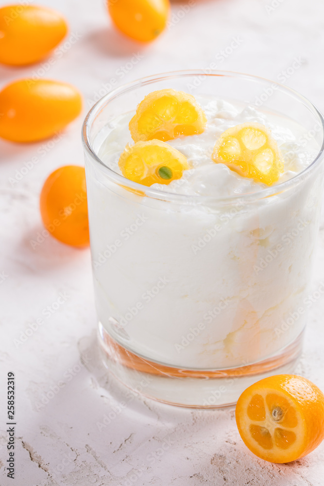 Close-up one transparent glass with yogurt with slices of exotic kumquat on white background. Close-up one transparent glass with yogurt with slices of exotic kumquat on white background.