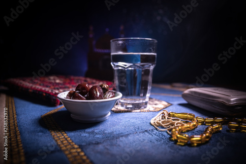 Water and dates. Iftar is the evening meal. View of decoration Ramadan Kareem holiday on carpet. Festive greeting card, invitation for Muslim holy month Ramadan Kareem. Dark background