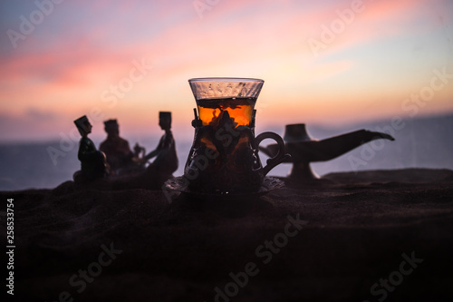 Arabic tea in traditional glass and pot on desert at sunset. Eastern tea concept. Artwork decoration on sand with tea.