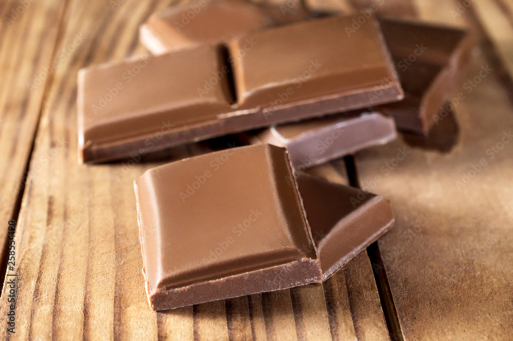 Fototapeta premium Pieces of chocolate bar on wooden table. Close up.