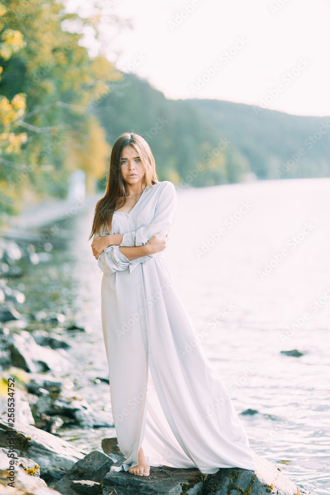 Girl in boudoir dress on the lake, standing and smiling. Unity with nature, morning bride in Russia. Beautiful eyes and model appearance Girl in boudoir dress on the lake, standing and smiling. Unity with nature, morning bride in Russia. Beautiful eyes and model appearance