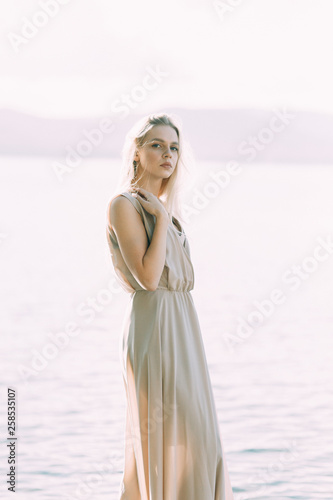 Girl in boudoir dress on the lake, standing and smiling. Unity with nature, morning bride in Russia. Beautiful eyes and model appearance