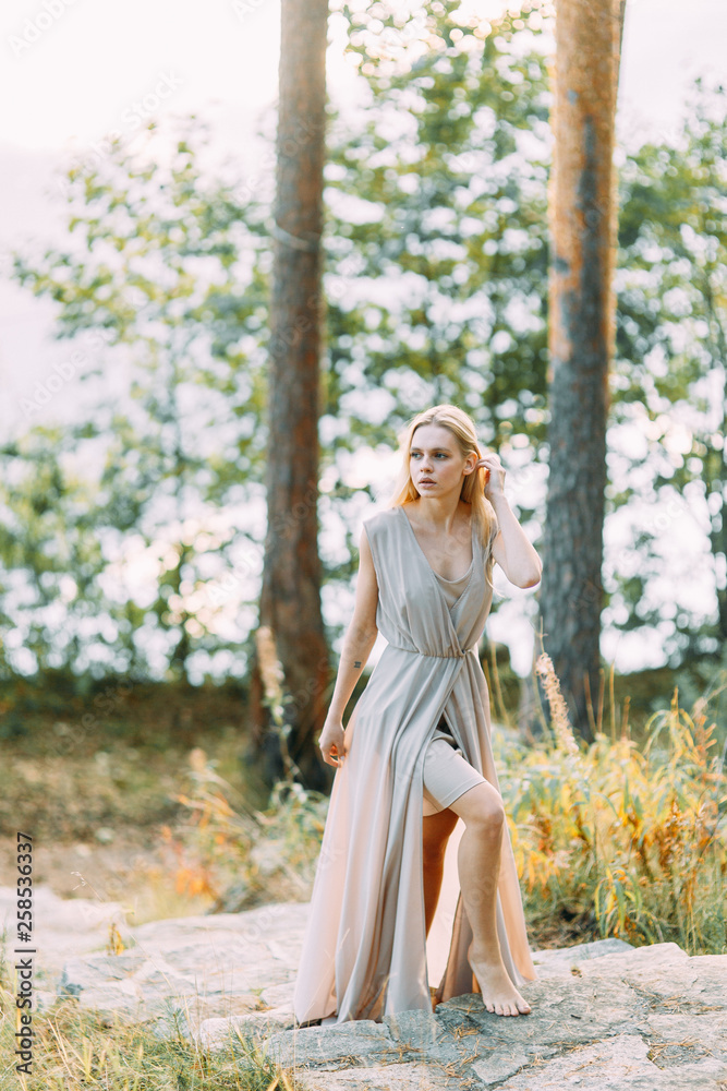 Girl in a boudoir dress in a pine forest. Standing on the rocks in a thin flying dress. Unity with nature at the wedding. Bride at sunset Girl in a boudoir dress in a pine forest. Standing on the rocks in a thin flying dress. Unity with nature at the wedding. Bride at sunset