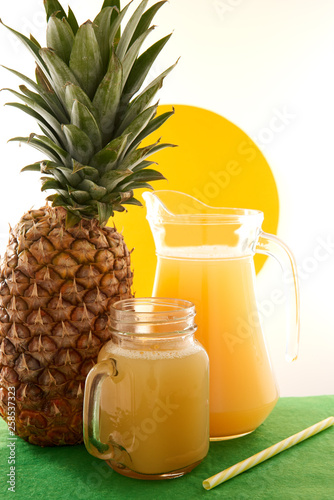 Jug and glass of pineapple juice with fruits on white background.